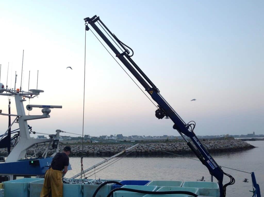 Grue de pêche Guerra : déchargement de poisson au port Pêcheur utilisant une grue Guerra M65.20A pour décharger du poisson frais sur un bateau au port.
