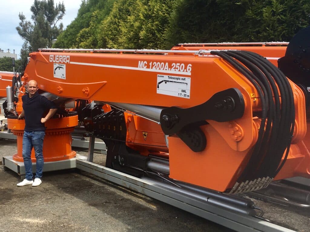 Grue télescopique Guerra MC 1200A.250.6 de haute précision Grue télescopique Guerra MC 1200A.250.6 orange avec un homme pour l'échelle et flexibles hydrauliques apparents.
